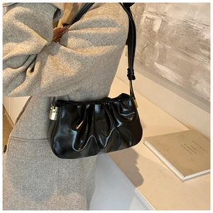 Detail of black glossy pleated cloud bag with elegant gold metal buckle and leather strap