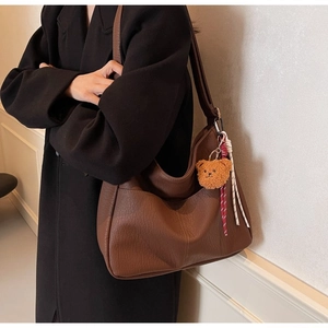 Detailed close-up of brown litchi grain leather bag with cute teddy bear charm accessory