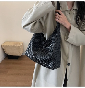 Detail of black woven leather hobo shoulder bag styled with a minimalist beige trench coat