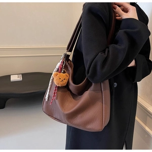 Detailed macro view of brown lychee-textured leather tote bag with cute bear charm