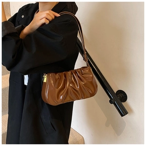 Brown pleated leather baguette bag worn by a model in a stylish black suit jacket