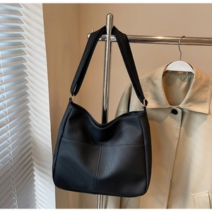 Detail of black pebbled leather hobo bag with wide strap hanging on a metal rack