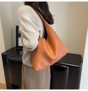 Large orange-brown tote bag with woven texture worn by model in an autumn lifestyle setting