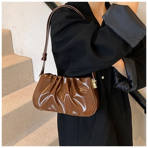Detailed side view of a dark brown pleated cloud bag with shiny leather and gold hardware