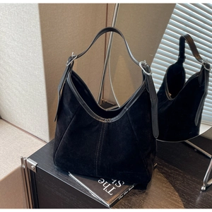 Detailed view of black suede tote bag with leather straps and silver buckles on wood table