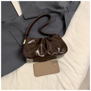 Detail of dark brown pleated cloud bag with shiny synthetic leather and gold hardware