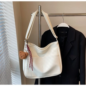 Detail of off-white oversized tote bag with plush bear charm and woven cord on metal hanger