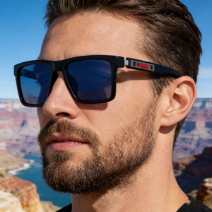 Detail of square sunglasses with blue lenses and red temple accents against a canyon backdrop