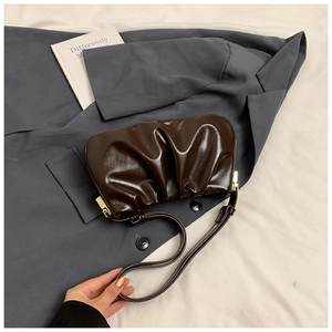 Detail of dark brown ruched cloud bag in glossy finish with gold metal buckles