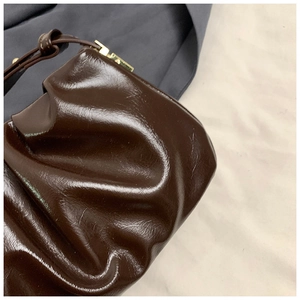 Close-up of deep brown pleated handbag with shiny finish and gold hardware detail