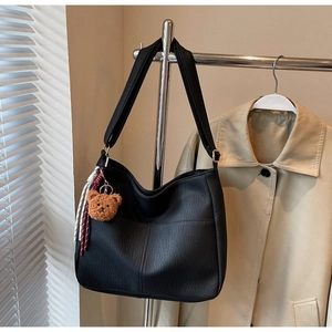 Detail of black pebbled leather tote bag with brown plush bear charm and woven cord