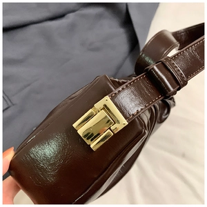 Close-up of a dark brown cloud bag with a glossy finish and a gold rectangular metal buckle