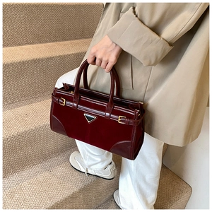 Close-up of deep burgundy glossy handbag featuring a triangle logo and leather straps
