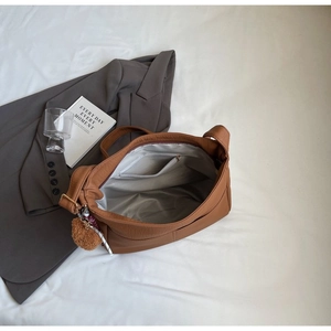Detail view of large brown leather tote bag with interior zipper pocket and plush charm