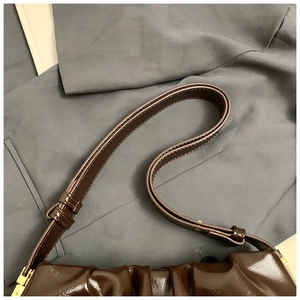 Detail of dark brown glossy patent leather cloud bag with pleated design and golden hardware