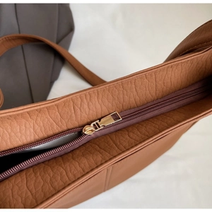 Detailed macro view of the smooth golden metal zipper and brown leather texture on a tote bag