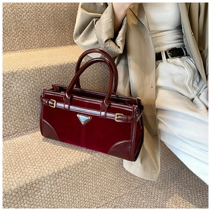 Detail of burgundy waxed leather tote bag featuring gold buckles and metal logo plaque