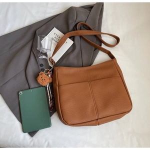 Detailed close-up of brown textured leather tote bag with functional pockets and bear charm