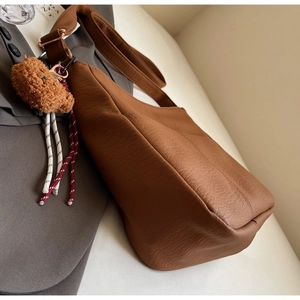 Close-up of brown pebbled leather tote bag with wide strap and plush bear charm