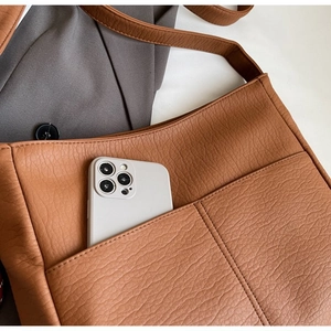 Close-up of brown textured leather shoulder bag showing front pockets with a smartphone