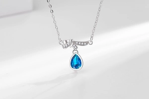 Detailed macro of a silver heart of the ocean necklace with a teardrop blue sapphire pendant