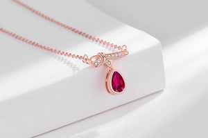 Detail of rose gold teardrop ruby necklace with diamond bowknot pendant design