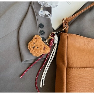 Close-up of a brown plush bear keychain charm on a vintage textured shoulder bag