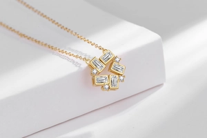Detail of gold necklace with geometric crystal pendant on a white marble pedestal