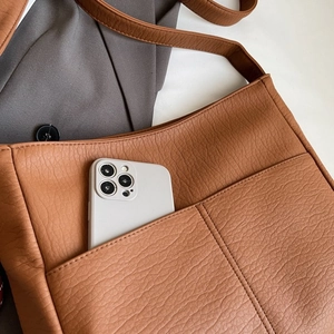 Macro view of brown lychee grain leather tote showing front pocket holding a smartphone