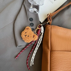 Detail of cute brown plush bear charm with striped tassel on litchi leather bag