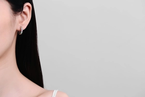 Close-up of small silver hoop earring with rainbow cubic zirconia on model's ear