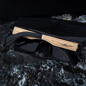 Detailed close-up of golden temples with green gemstone and relief on black square sunglasses