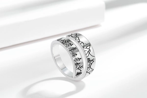 Detail of silver couple rings with mountain and forest engraving on white podium