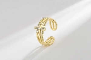 Macro detail of adjustable gold-colored triple-layered rope ring with a sparkling cross