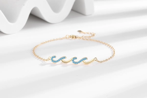 Close-up of golden wavy bracelet with blue zircons and lobster clasp on white surface