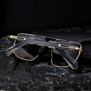 Detail of square frame sunglasses with black and gold temples on a textured rock base