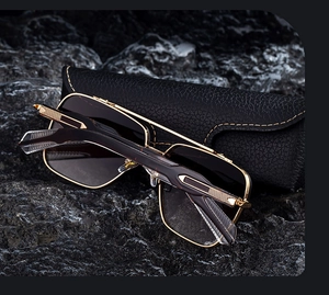 Detail of square double-bridge sunglasses with textured gold temples on black stone