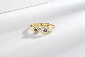Dettaglio ravvicinato dell'anello infinito dorato con zirconi viola a cuore e micro-diamanti