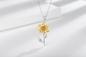Close-up of sunflower pendant with golden petals and orange gemstones on silver chain