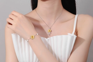 Detail view of sunflower necklace and pearl bracelet set on model with white pleated dress