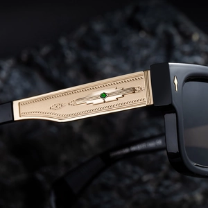 Detail of square sunglasses with gold engraved temples and green gemstone inlay