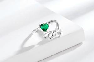 Detailed close-up of double dolphin open ring with green heart stone and forever engraving