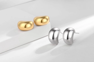 Detailed view of 18K gold and silver hollow C-shaped earrings on stone steps