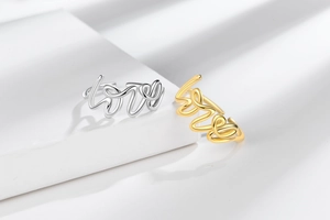 Close-up of gold and silver Love script rings displayed on minimalist white geometric steps