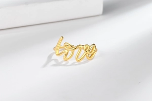 Macro detail of the golden LOVE script ring showing smooth polished metallic texture