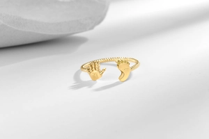 Detailed view of adjustable gold ring featuring small hand and crystal foot designs