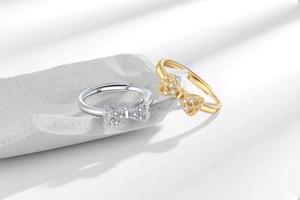 Detail of silver and gold bow rings with micro-set zircon on light stone surface