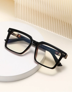 Detail of black square optical frame with gold dots on a minimalist white stand