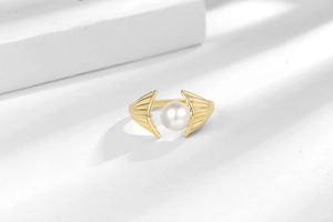Macro detail of gold-plated shell ring featuring a lustrous pearl in artistic lighting