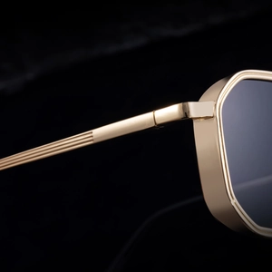 Detailed close-up of golden metal hinges and textured temple of square sunglasses